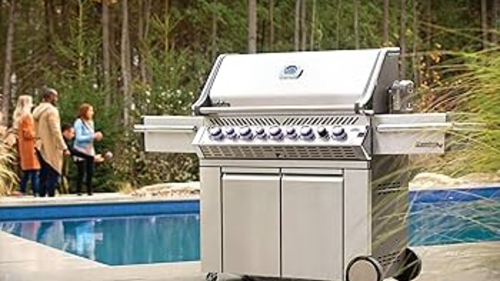 Napoleon stainless gas grill on a cart beside a backyard pool